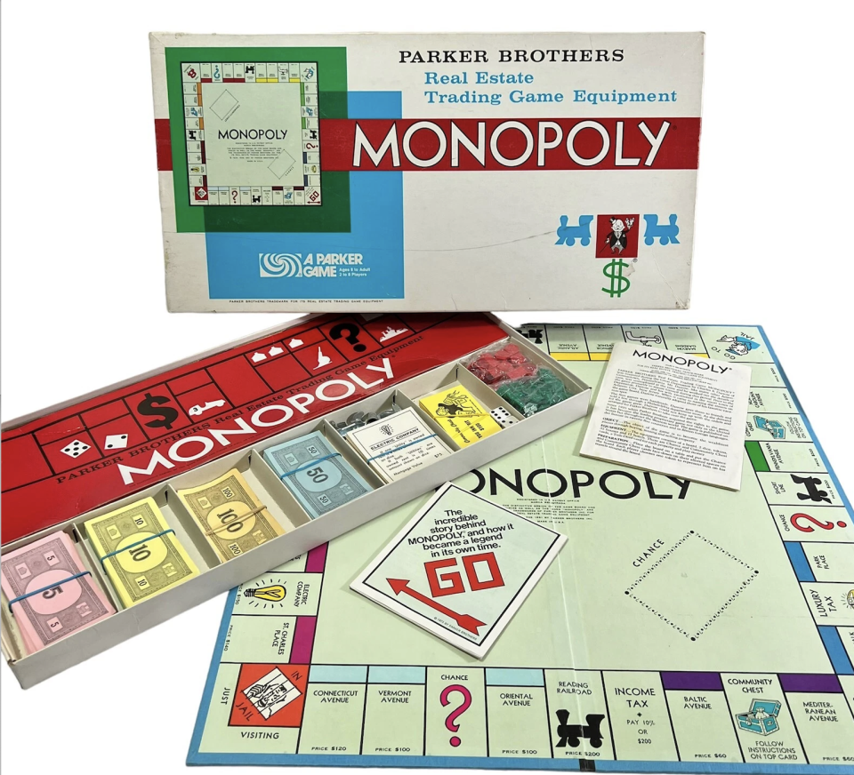 A vintage Parker Brothers Monopoly set with its box, board, money, and pieces laid out, showing GO, Chance, and property spaces like Baltic and Mediterranean Avenue.
